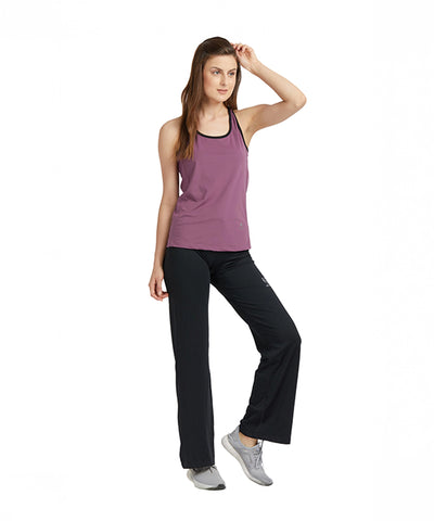 Woman wearing a Mauve Sleeveless Tee with Back Straps, black pants, and gray sneakers poses against a white background.
