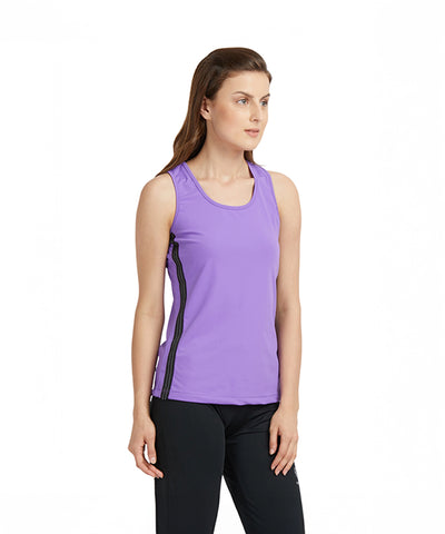 Woman wearing a purple round neck sleeveless top and black pants standing against a plain white background.