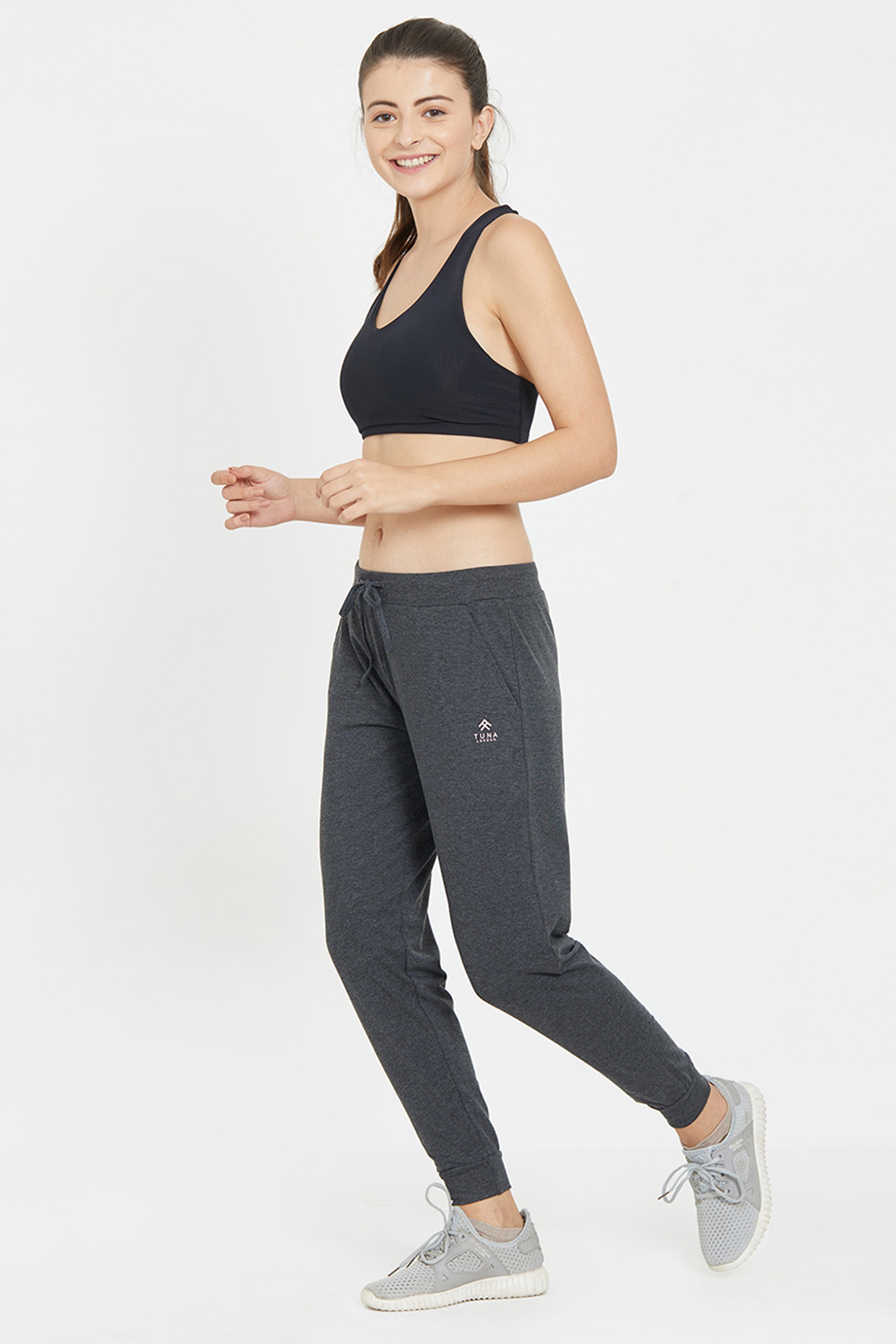 Smiling woman in a black sports bra and Classic Joggers 81 with an adjustable fit poses in a jogging stance against a white background—ideal for active days or relaxed lounging.