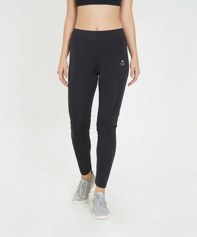 A woman wears Black Poly Blend Tights for Women - LG10 with a high-rise waistband, grey sneakers, and a black sports bra on a white background—ideal for workout essentials.