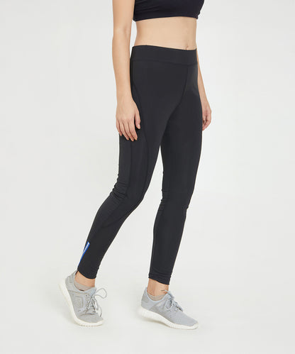 A woman stands against a white background wearing Black Poly Blend Tights for Women - LG10 with a high-rise waistband and gray sneakers—ideal for your workout essentials.
