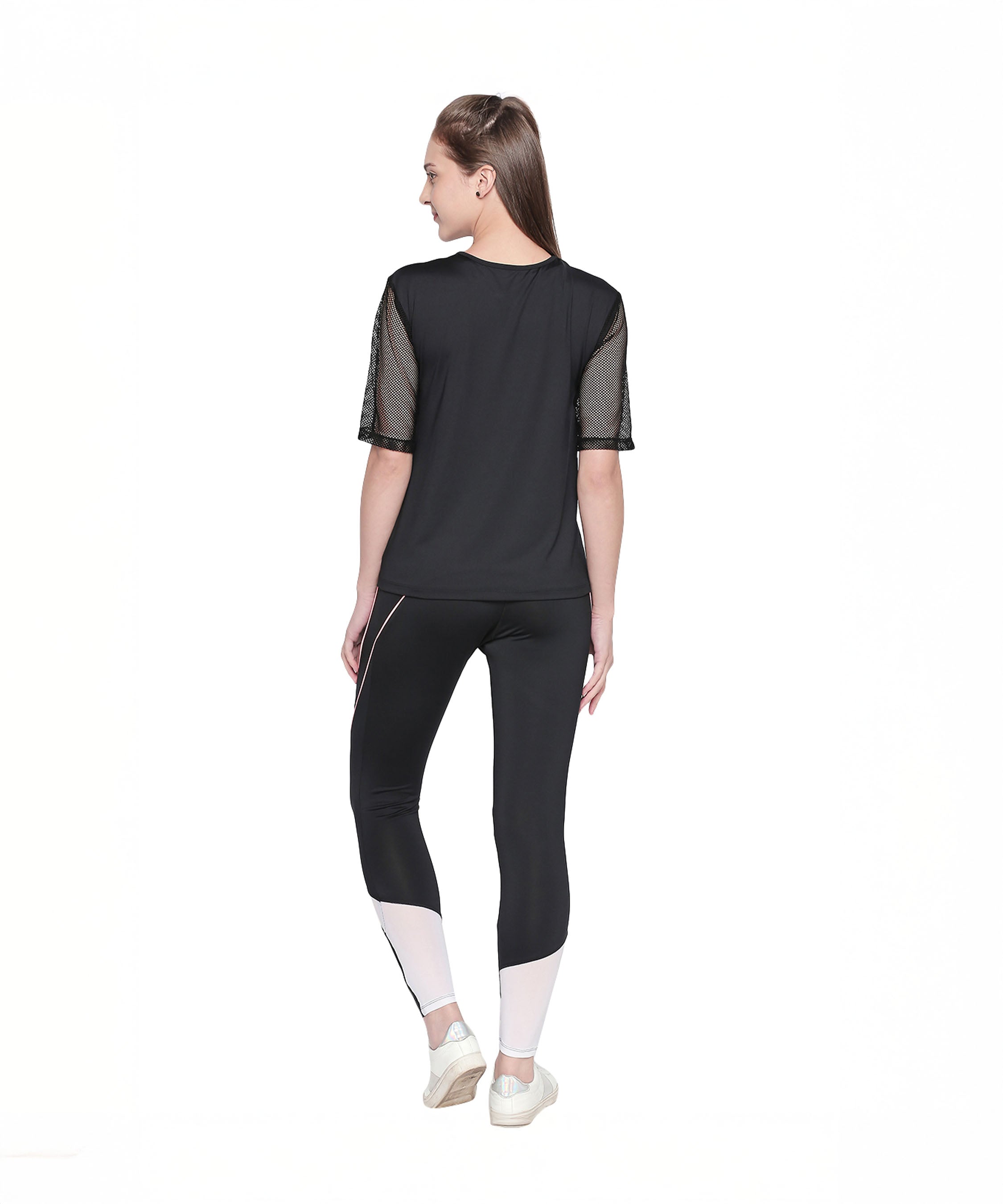 A woman stands facing away, wearing a black top and the Black High Waisted Leggings - G12 featuring white geometric panels, set against a white background.