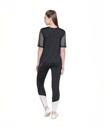 A woman stands facing away, wearing a black top and the Black High Waisted Leggings - G12 featuring white geometric panels, set against a white background.