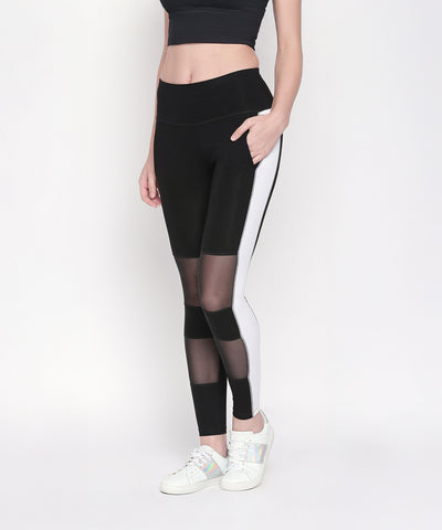 A woman wears the Black and White High Waisted Leggings - LG13, featuring white side panels and mesh inserts, styled with a black crop top and white sneakers. These high-rise leggings offer a chic, sporty look for any workout.
