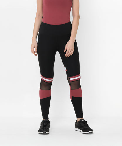 Woman wearing Sienna Black High Waisted Leggings with mesh panels, a maroon top, and black sneakers, standing.