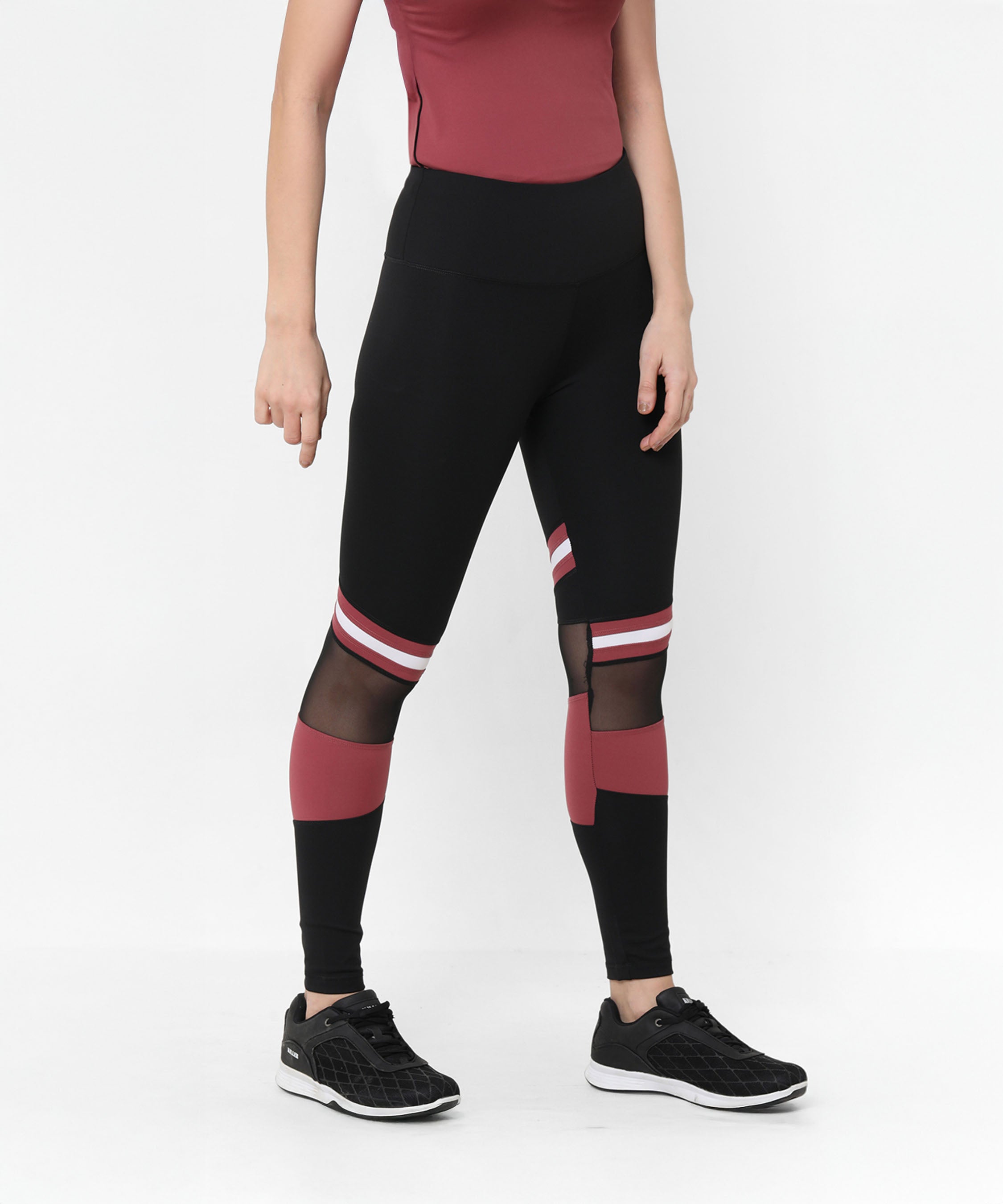 A woman wearing Sienna Black High Waisted Leggings with red and white stripes, mesh panels, and black sneakers stands against a white background. The four-way stretch fabric offers comfort and flexibility for any activity.