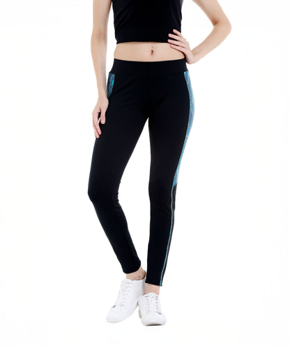 A woman wears Black Sports Leggings G1—black leggings with blue side stripes and an elasticated waistband—paired with a black crop top and white sneakers, standing against a white background.