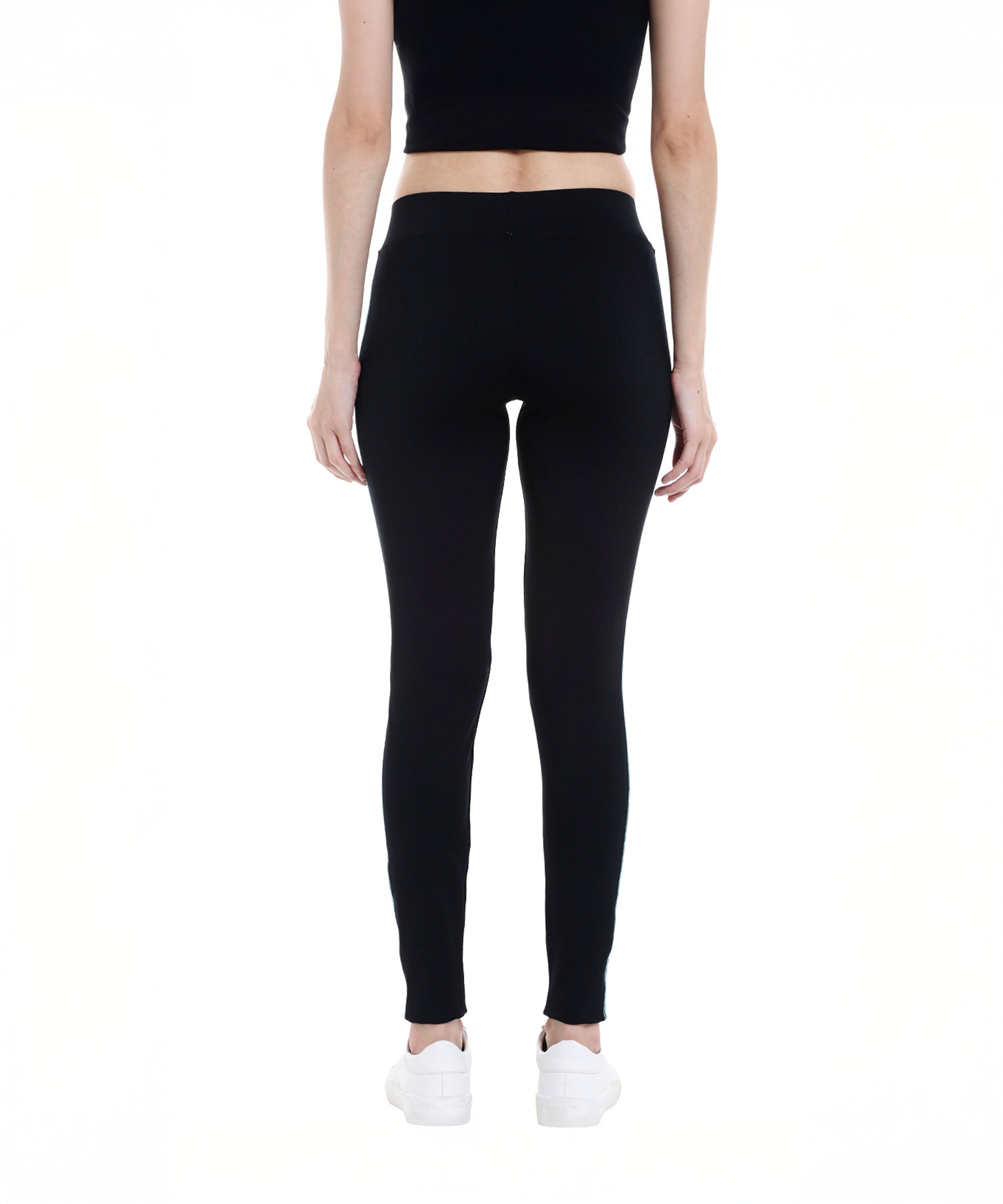 A woman stands facing away on a white background, wearing the Black Sports Leggings G1 with an elasticated waistband, a black top, and white sneakers.