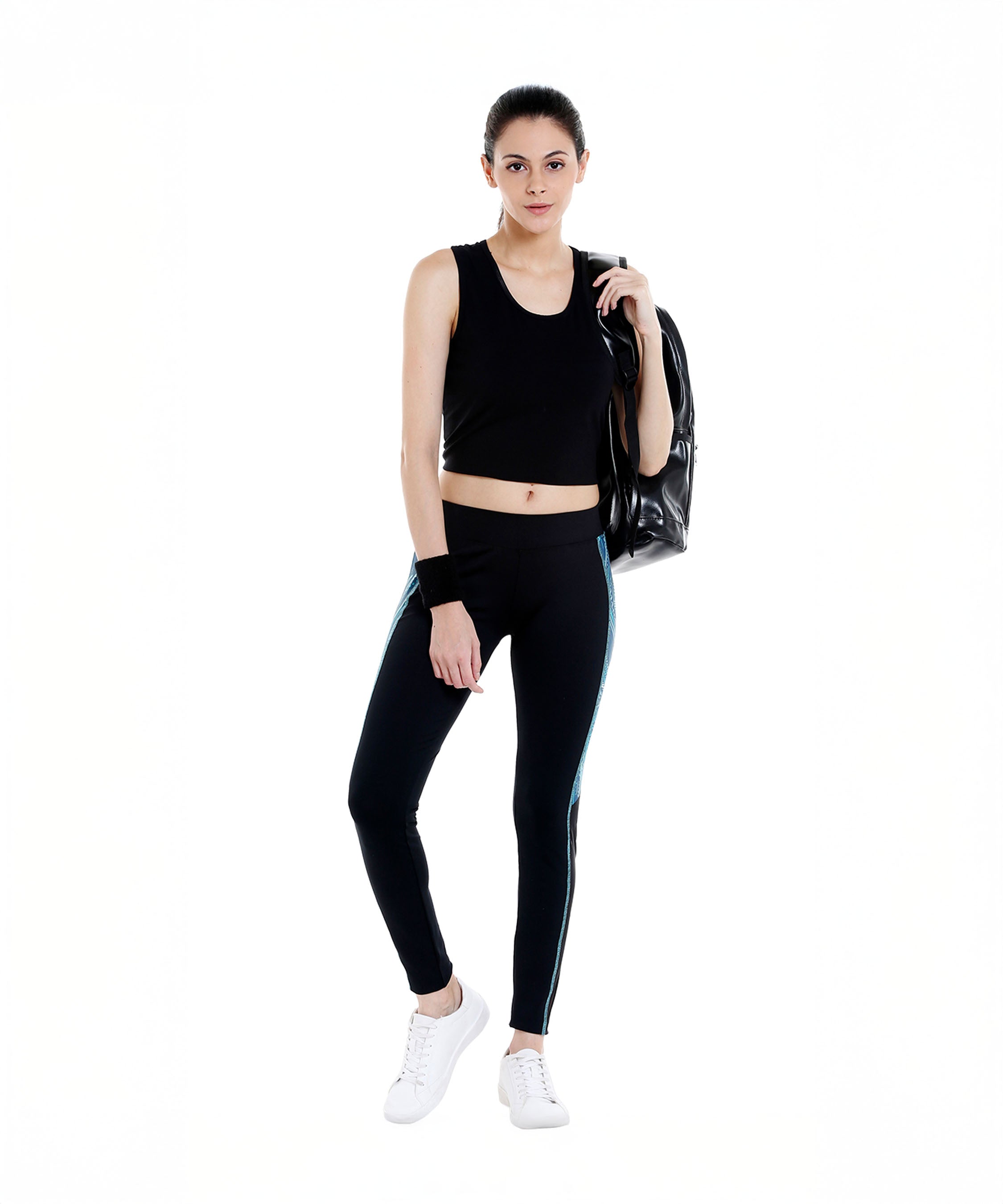 A woman wearing Black Sports Leggings G1 with an elasticated waistband and white sneakers, holding a bag over her shoulder, stands against a white background.