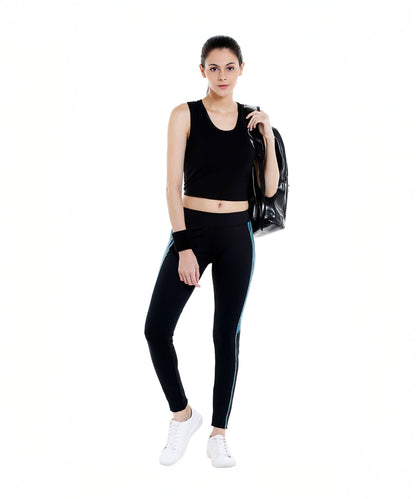 A woman wearing Black Sports Leggings G1 with an elasticated waistband and white sneakers, holding a bag over her shoulder, stands against a white background.