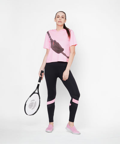 A woman in the Black High Waisted Compression Legging With a Neon Pink Patch holds a tennis racket and stands confidently against a white background.
