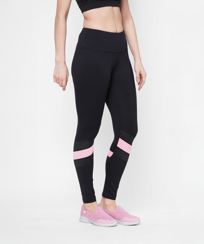 A woman models the Black High Waisted Compression Legging With a Neon Pink Patch and matching pink shoes, standing against a white background. Four-way stretch compression fabric provides a flattering, comfortable fit.