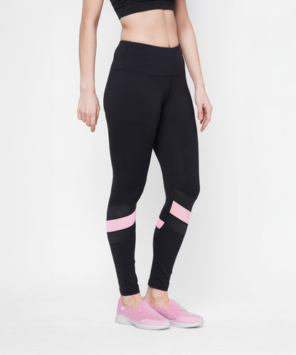 A woman models the Black High Waisted Compression Legging With a Neon Pink Patch and matching pink shoes, standing against a white background. Four-way stretch compression fabric provides a flattering, comfortable fit.
