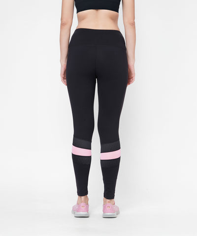 Woman wears the Black High Waisted Compression Legging With a Neon Pink Patch, featuring four-way stretch compression fabric for comfort and support, paired with a black crop top as she stands facing away.