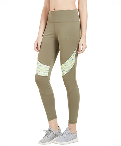 A person is wearing Militiary Sports Leggings in olive green with patterned panels, paired with gray sneakers, and standing against a white background.