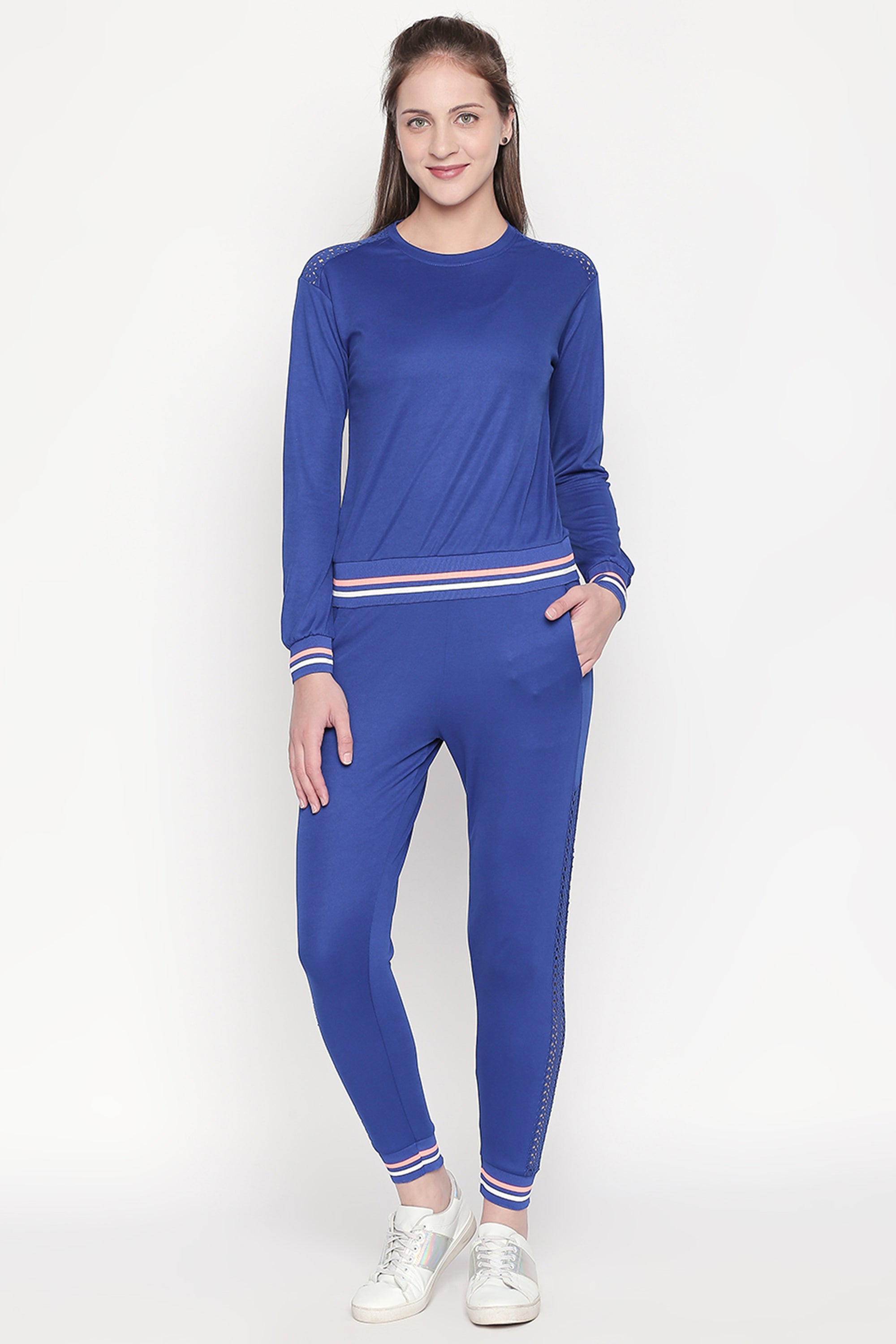 A woman stands and smiles against a plain light background, wearing Classic Blue Joggers paired with white sneakers.