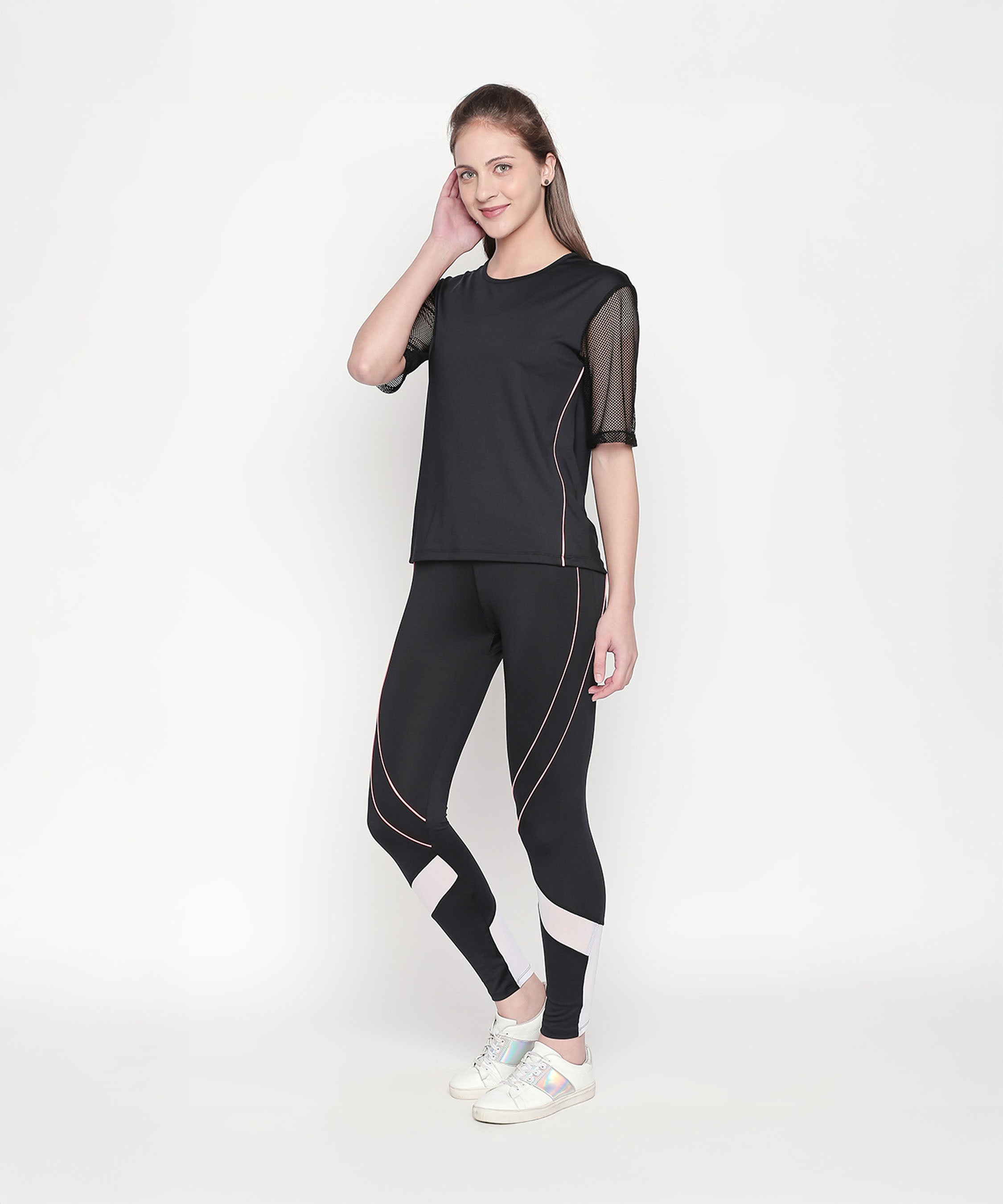 A woman poses confidently against a white background in the Activewear Black Tracksuit, featuring high waisted, moisture-wicking leggings and white sneakers.