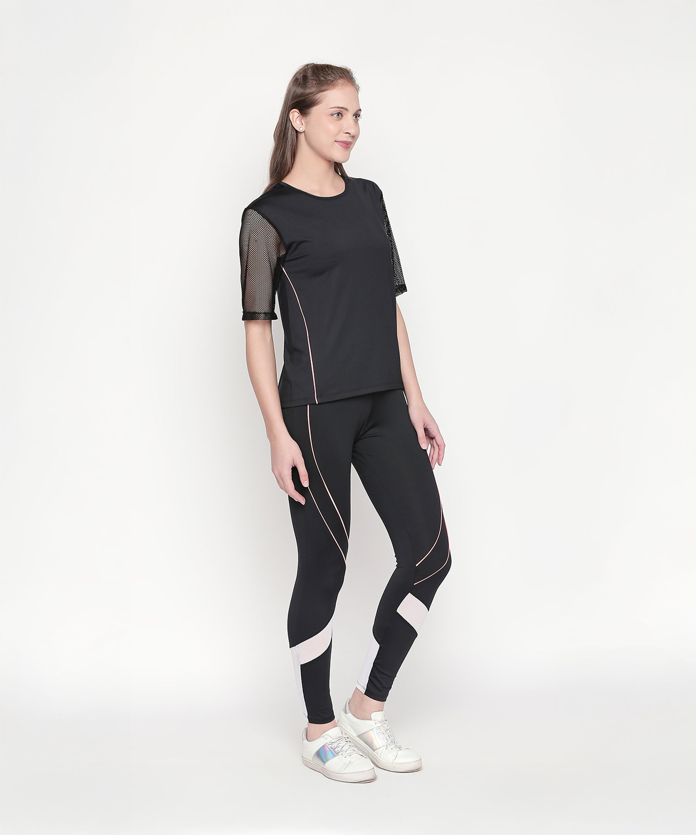 Woman in a Black Loose Fit Round Neck Net Half Sleeve Top and white sneakers poses confidently against a plain white background.