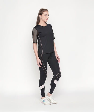 Woman in a Black Loose Fit Round Neck Net Half Sleeve Top and white sneakers poses confidently against a plain white background.