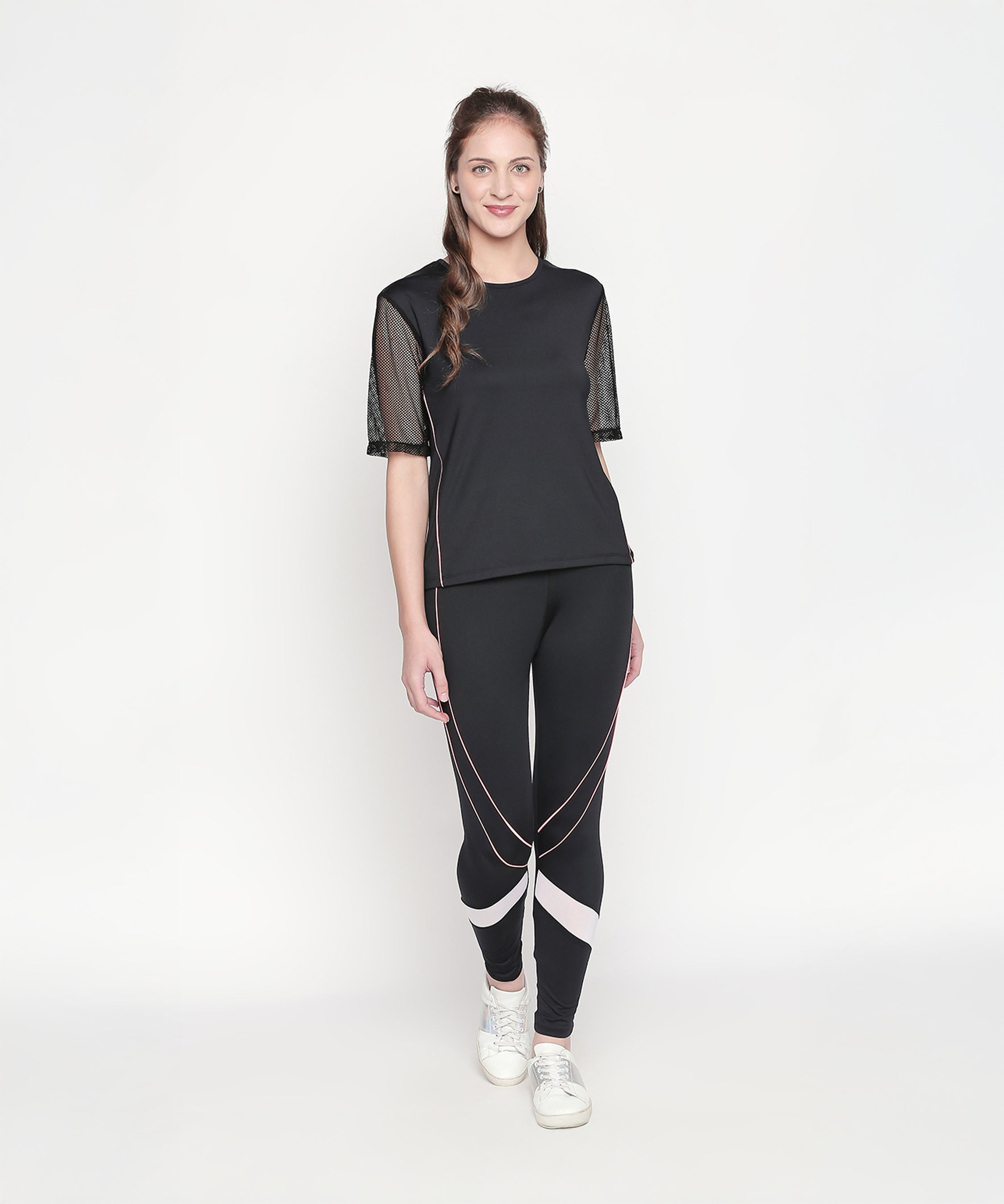 A woman wears the Activewear Black Tracksuit with high-waisted leggings and mesh sleeves, paired with white sneakers, against a plain white background. Moisture-wicking fabric ensures comfort during any workout.