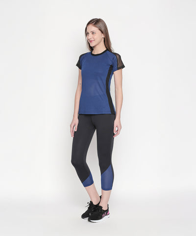 A woman stands against a plain white background wearing Black High Waisted Leggings 74 featuring blue mesh panel details and black sneakers.