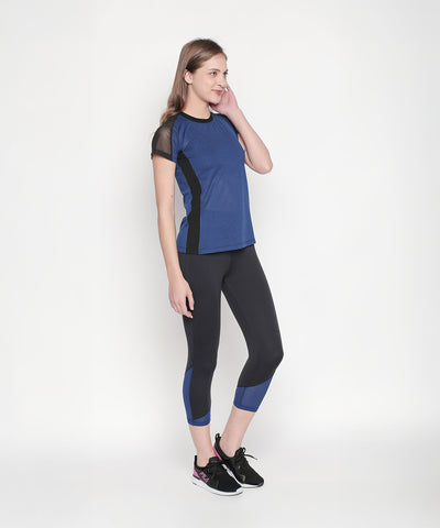Woman in black high waisted leggings stands against a white background, touching her face and smiling.