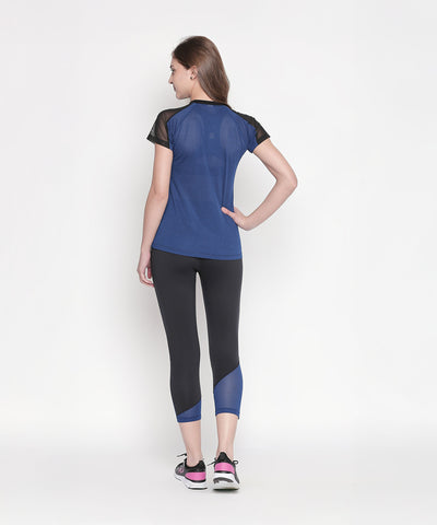 A woman stands facing away, hand on hip, wearing the Blue - Textured Top With Net Sleeves and black leggings against a white background. Moisture-wicking fabric keeps her comfortable during any activity.