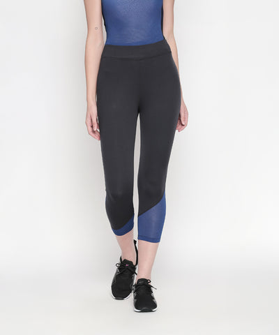 Woman wearing regular fit black and blue athletic leggings, Blue - Textured Top With Net Sleeves featuring moisture-wicking fabric, and black sneakers, standing against a white background.