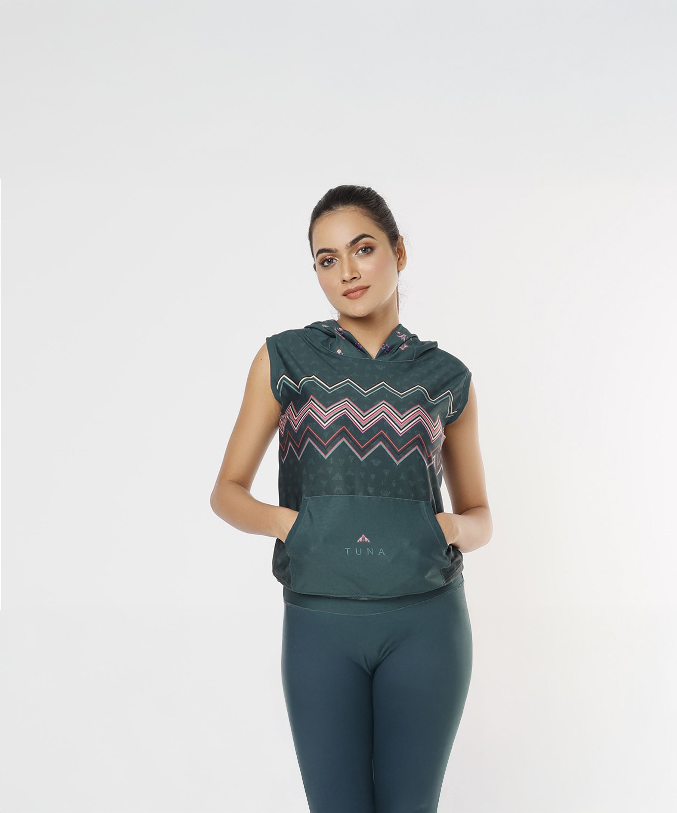 A woman poses against a plain white background, modeling the Tuna Active Teal Hooded Top with matching leggings—showcasing stylish workout wear.