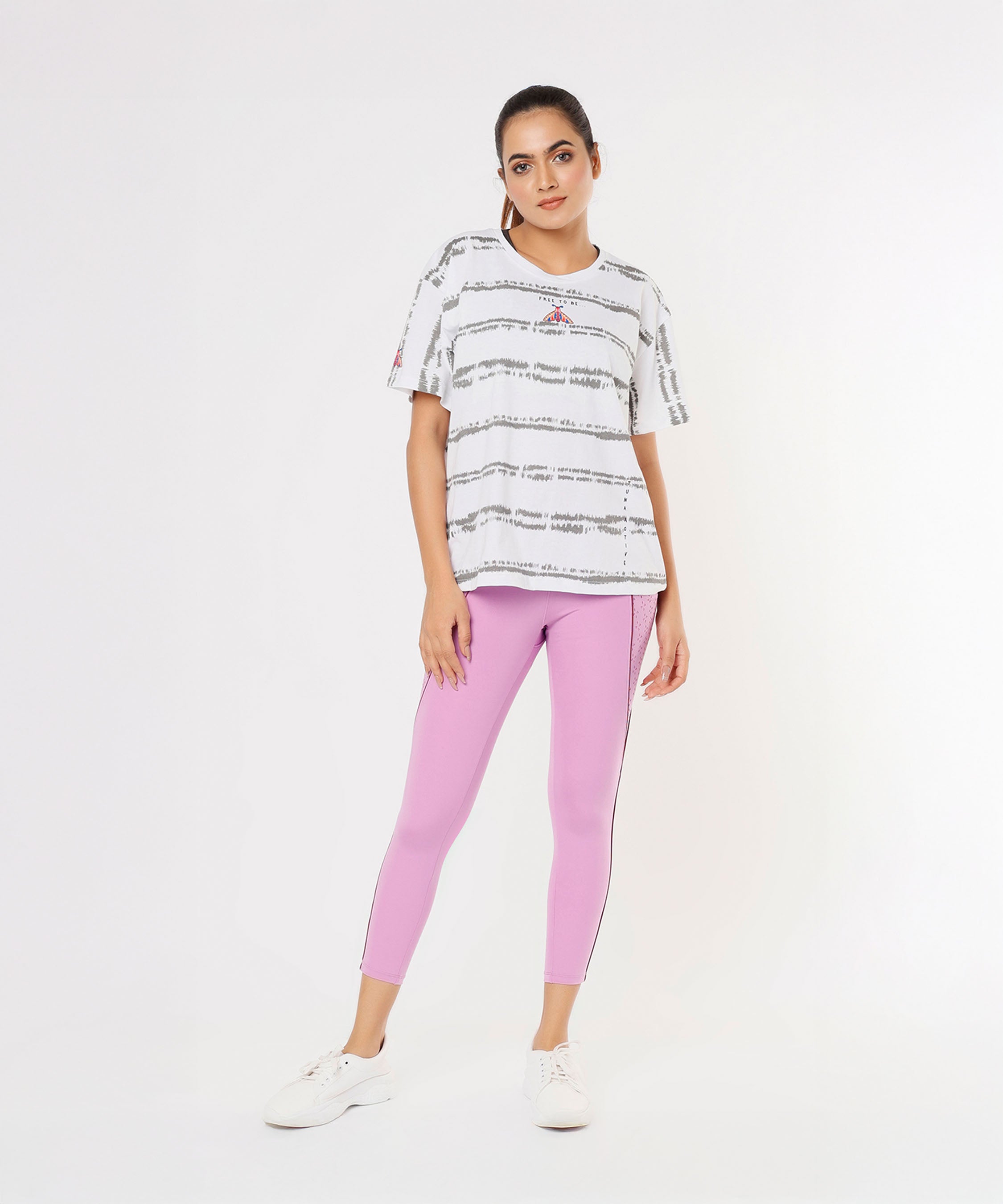 Woman wearing Tuna Active Pink Lilac Leggings with a laser cut pocket and a white and gray striped t-shirt, standing against a plain white background.