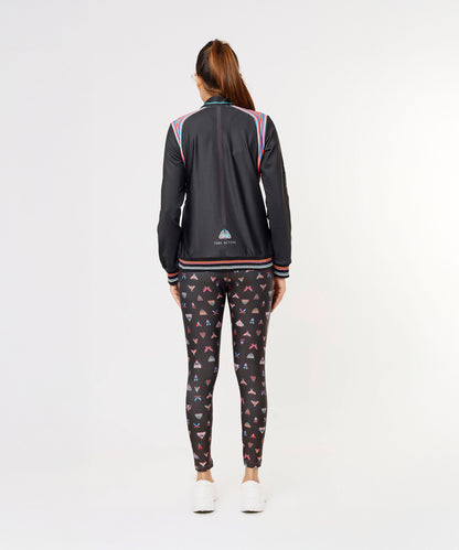 Woman standing facing away, wearing the Tuna Active Black Bomber Jacket with patterned leggings and white sneakers.