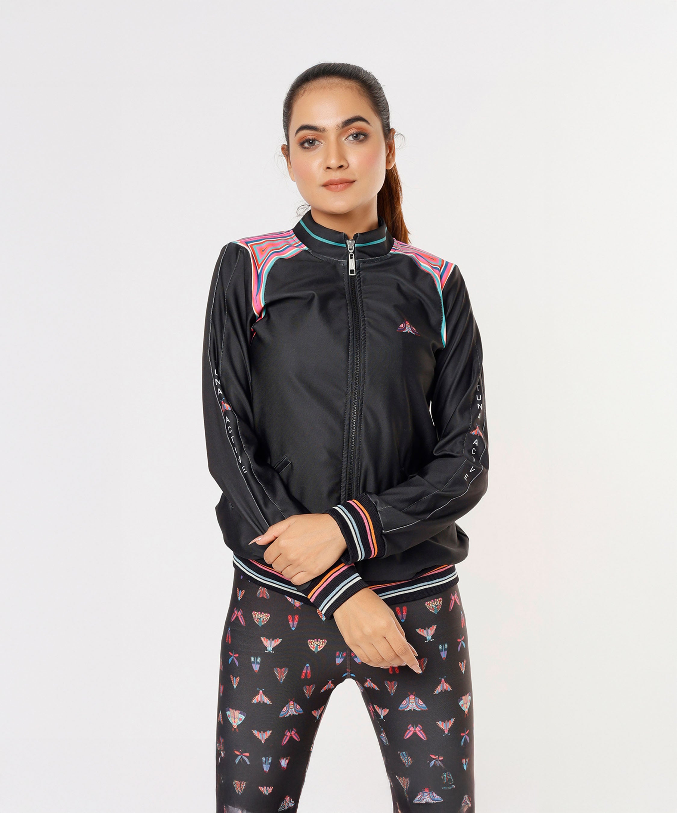 Woman in a Tuna Active Black Bomber Jacket and patterned leggings stands against a plain white background.