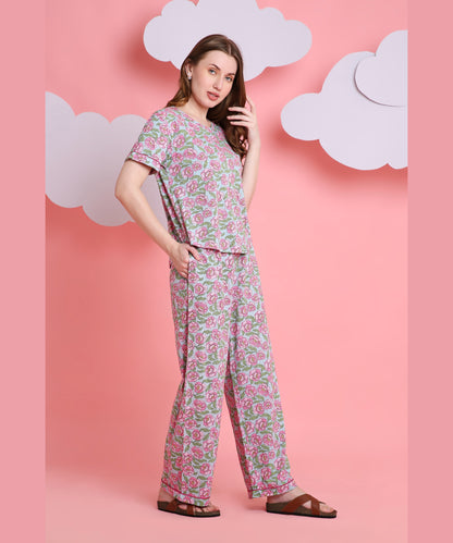 A woman wearing the Floral Love night suit, made from breathable fabric, and sandals poses against a pink background with paper clouds.
