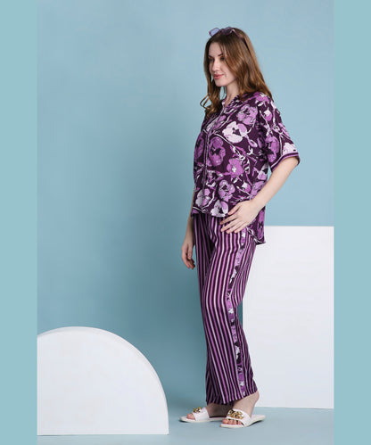 A woman models the Purple Breeze pyjama set—featuring floral and striped designs—while standing sideways against a blue background in white sandals, showcasing a fresh, stylish approach to women’s loungewear.