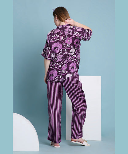 A woman models the Purple Breeze pyjama set, featuring floral and striped designs, as she stands facing away against a blue background.