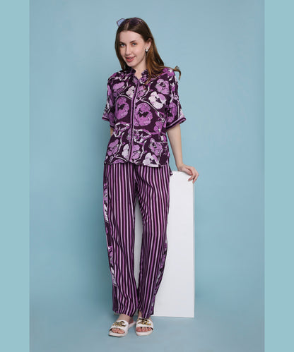 A woman smiles in comfortable loungewear, wearing the Purple Breeze pyjama set with matching purple floral and striped patterns, standing against a blue background.