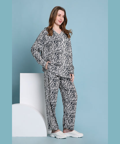 A woman stands against a blue backdrop with geometric props, wearing the relaxed fit Zeba zebra print pyjama set and white shoes.