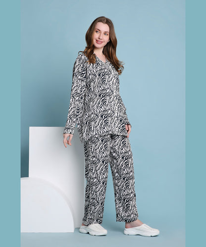 Smiling woman wears the Zeba relaxed fit zebra print pyjama set with white slip-on shoes, posing against a blue background.