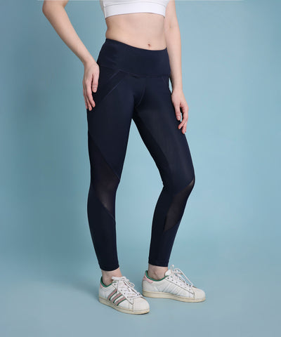 Woman wearing Indigo poly blended leggings, a white crop top, and white sneakers stands against a light blue background.