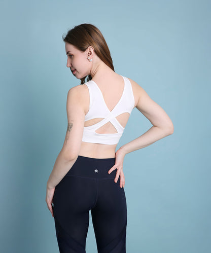 Woman wearing the White Sports Bra featuring moisture-wicking fabric and a crisscross back, paired with black leggings, posing against a blue background.