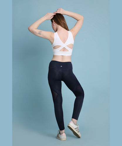 Woman in activewear posing with hands on head, wearing a white sports bra and Indigo poly blended leggings.