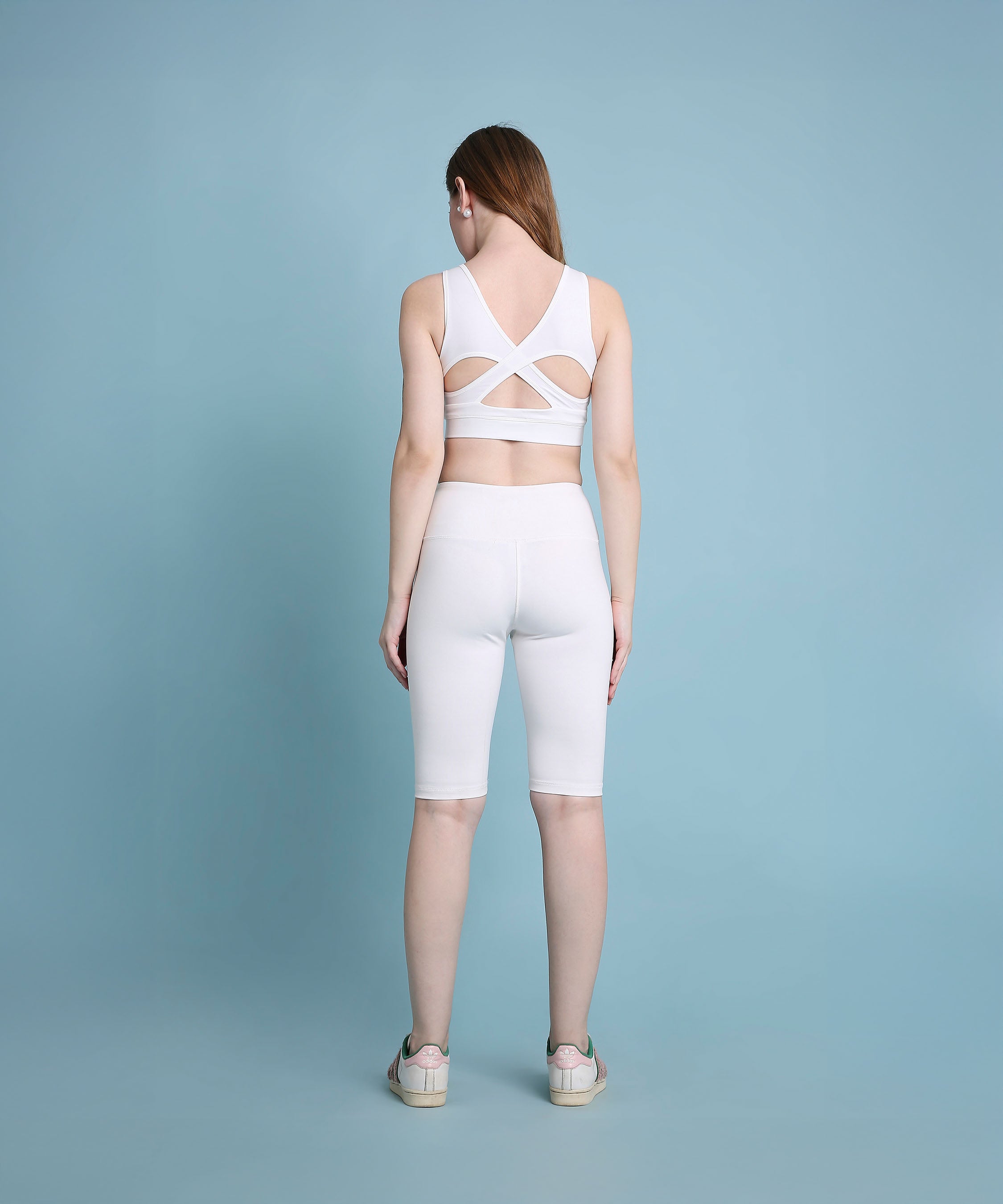 A woman wearing the White Sports Bra, designed with medium support and moisture-wicking fabric, stands facing away against a light blue background.