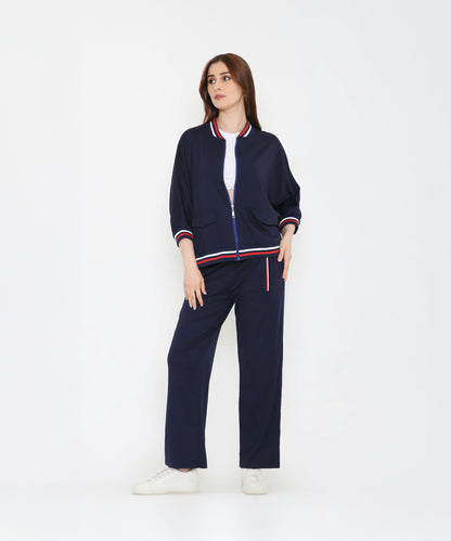 A woman in a Navy Blue Zipped Long Jacket with Tracks and white sneakers stands with one hand in her pocket against a white background.