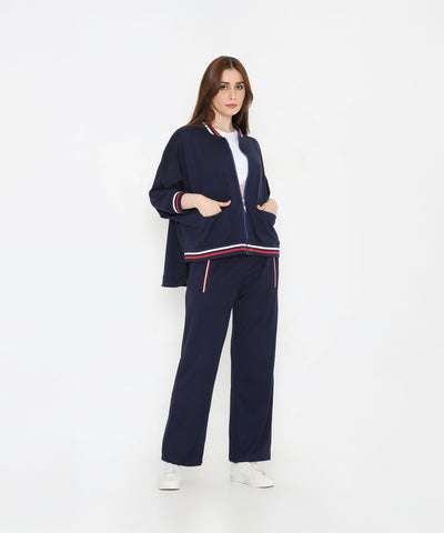 Woman in a Navy Blue Zipped Long Jacket with matching tracks, accented by red and white stripes. Features pockets for convenience—stylish women's activewear ideal for comfort and paired perfectly with white sneakers.