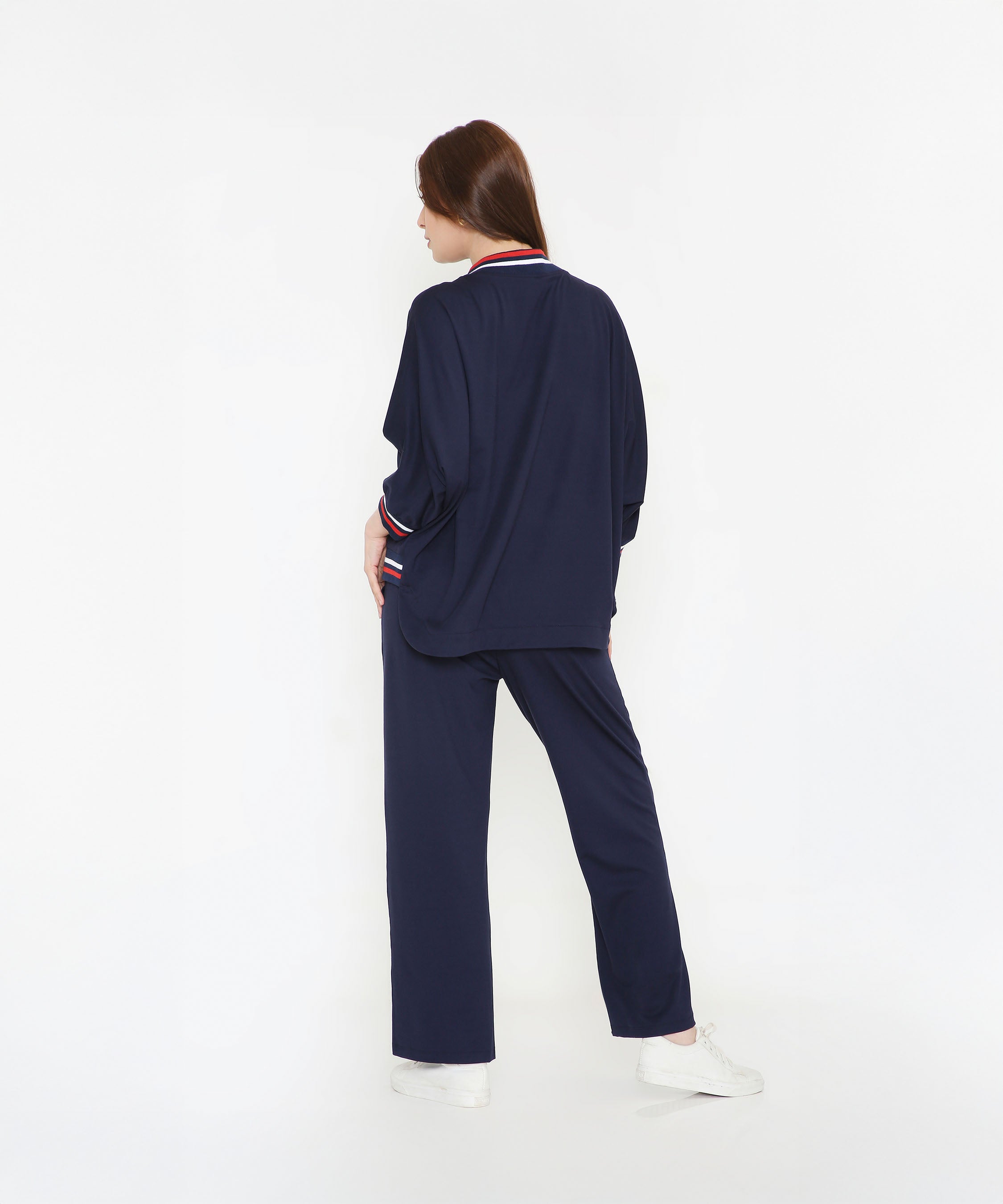 A woman wears the Navy Blue Zipped Long Jacket with Tracks, styled as a chic women's activewear set. She stands facing away from the camera against a white background, paired with white sneakers.
