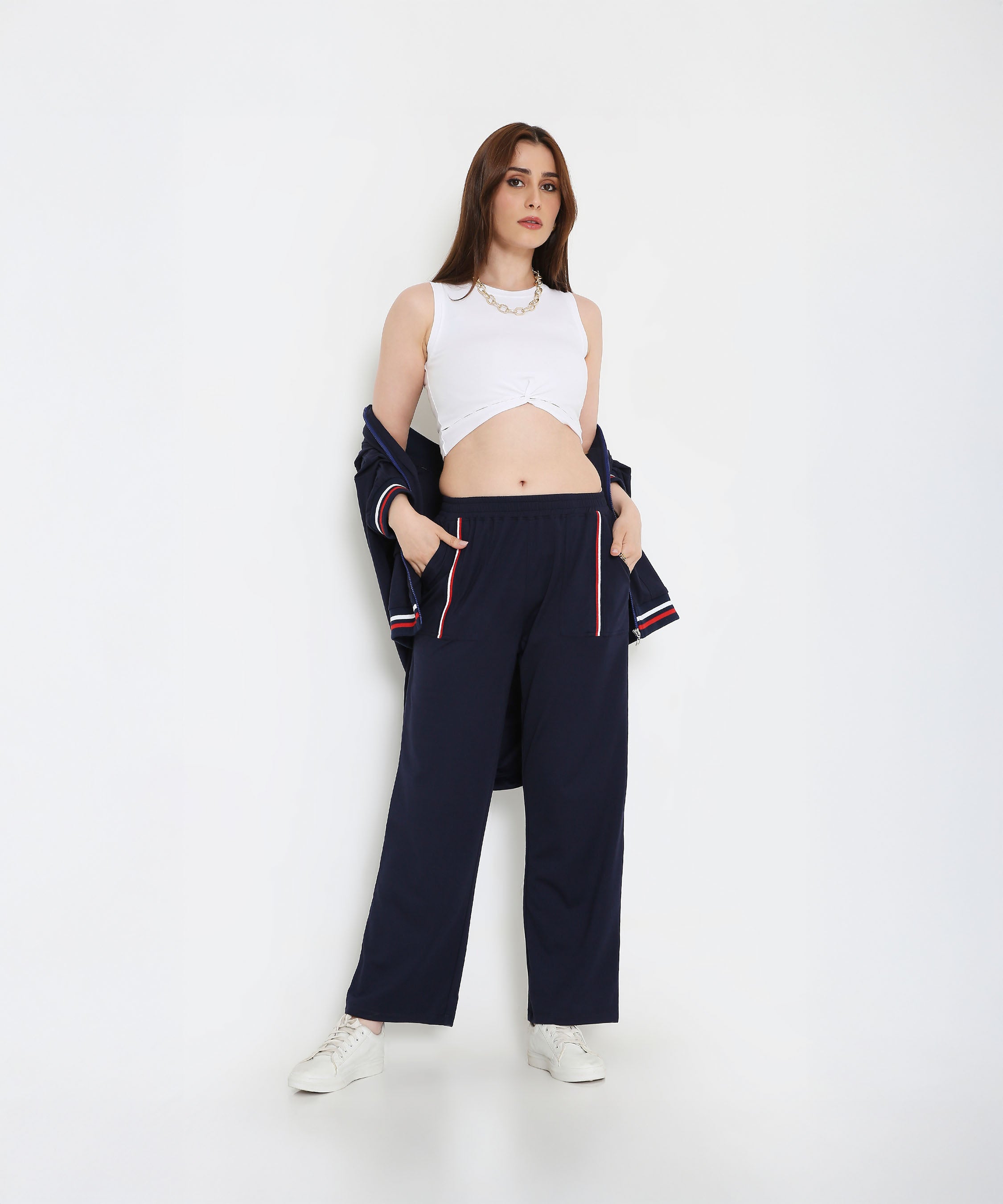 Woman in a white tank top and Navy Blue Zipped Long Jacket with Tracks, hands in pockets, white sneakers—a chic and effortless look in women’s activewear.