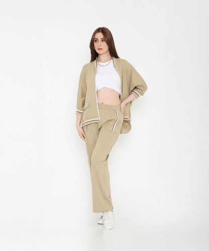 Woman in a Beige Zipped Long Jacket with Tracks and sneakers poses against a plain white background, showcasing chic style paired with the comfort of women’s activewear.