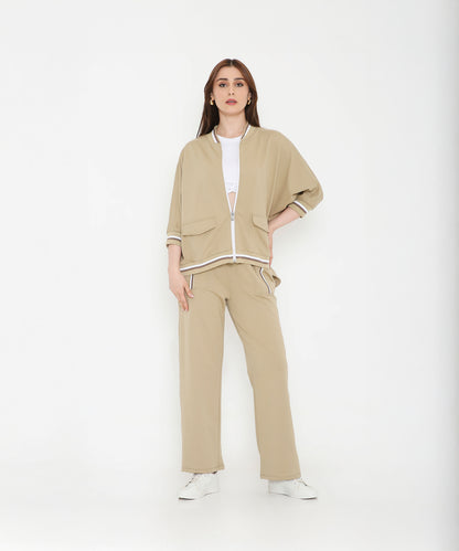 Woman wearing a Beige Zipped Long Jacket with Tracks, styled with a white crop top and sneakers, stands against a white background.