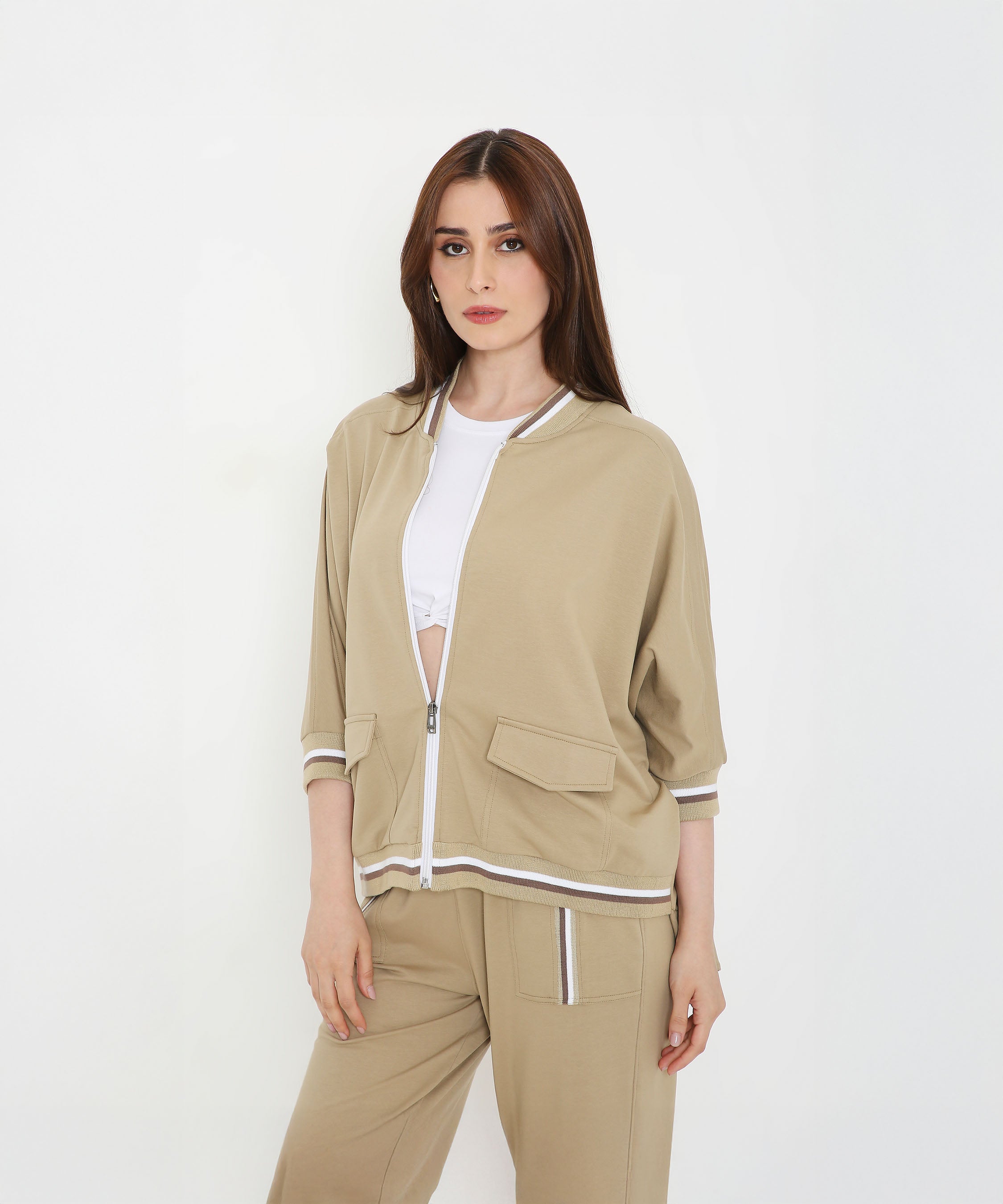 A woman wearing the Beige Zipped Long Jacket with Tracks, styled as an activewear set over a white top, stands against a white background.