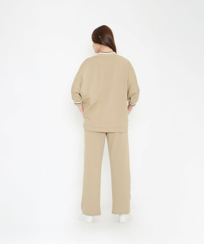 Woman facing away, dressed in the Beige Zipped Long Jacket with Tracks and white sneakers, standing against a white background.